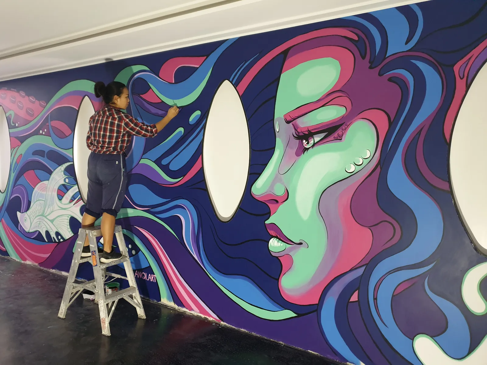 Anqi painting a large mural of a woman's face
